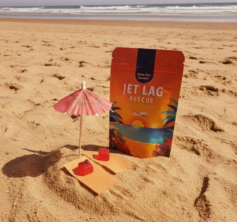 Packaged product labeled 'Jet Lag Rescue' on a sandy beach with a small umbrella and cookies.
